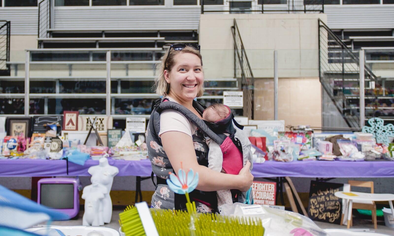 Two masked moms—one holding a child with a mask, the other pregnant—shop for their families at the local JBF sale.